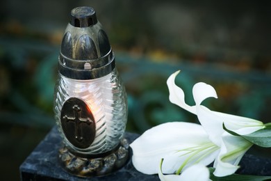 Lilies and grave lantern with burning candle on tombstone in cemetery