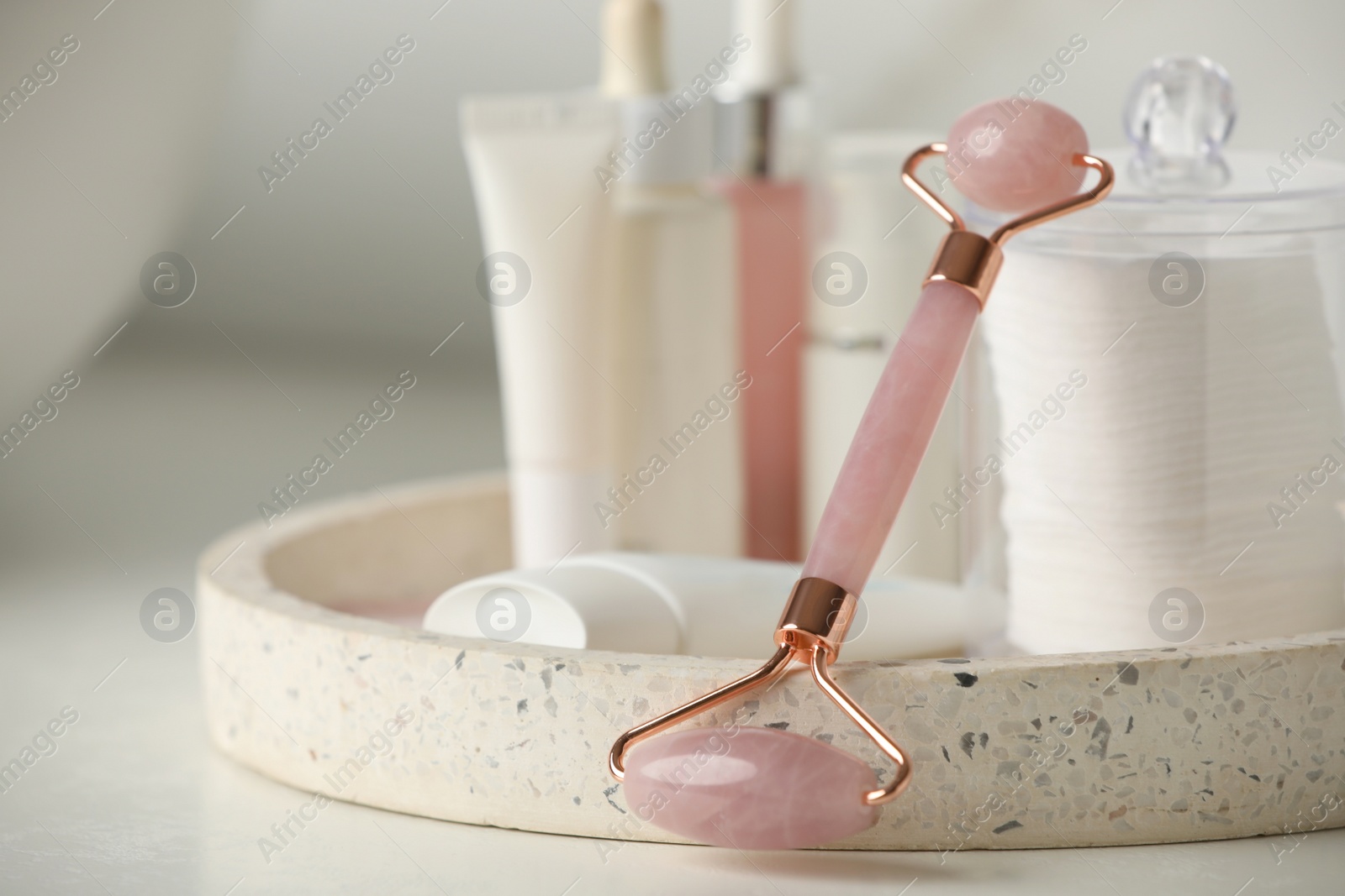 Photo of Natural face roller and tray with cosmetic products on white table, closeup