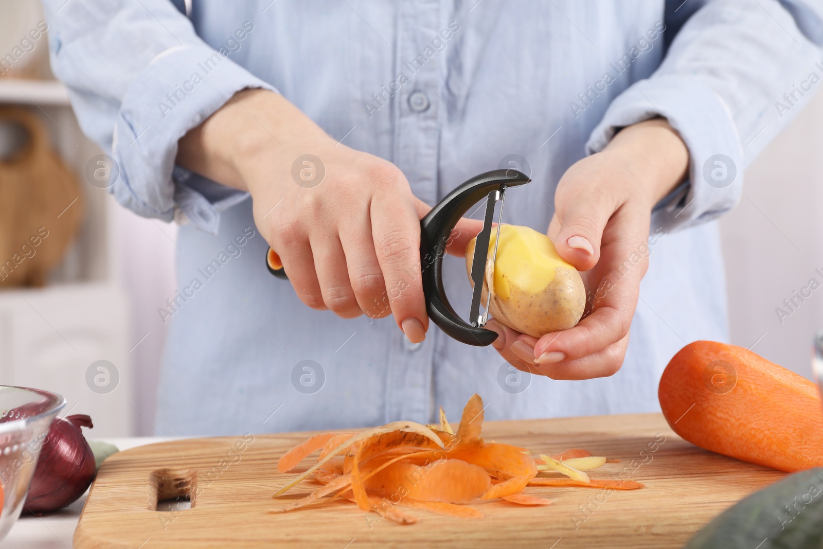 Photo of Woman peeling fresh potato at table indoors, closeup