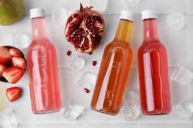 Photo of Tasty kombucha in glass bottles, fresh fruits and ice on white table, flat lay