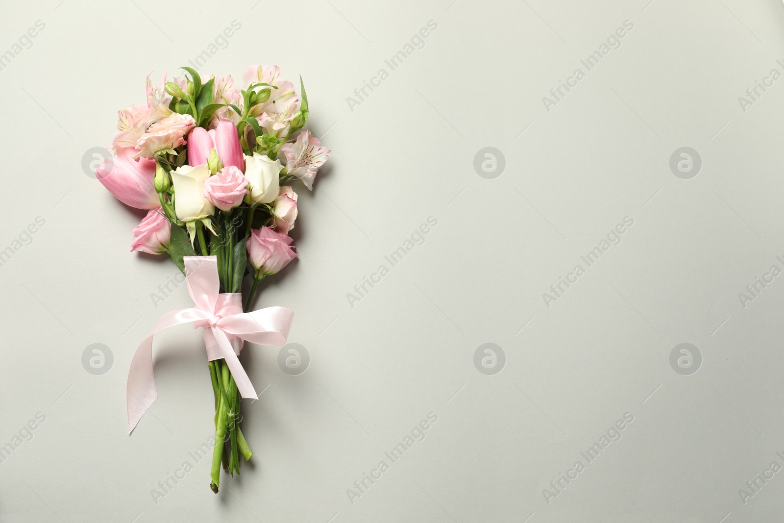 Photo of Happy Mother's Day. Bouquet of beautiful flowers tied with pink ribbon on light grey background, top view. Space for text