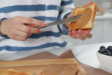 Woman spreading tasty nut butter onto toast at table, closeup