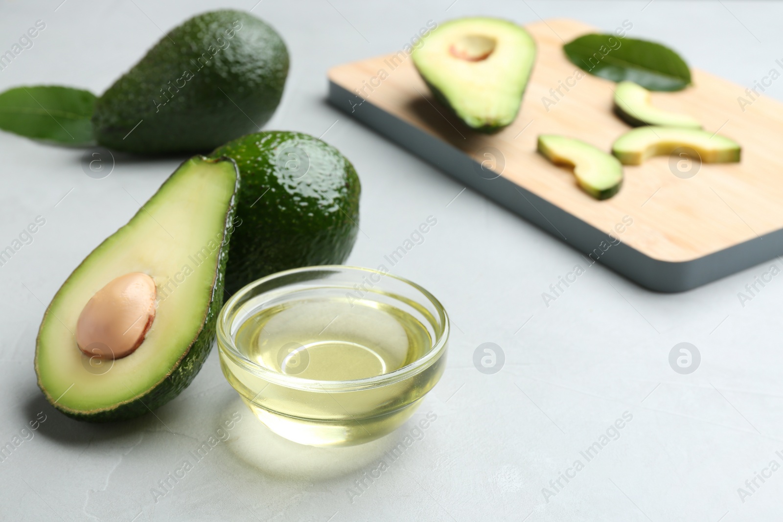 Photo of Bowl of natural oil and avocados on grey stone background. Space for text