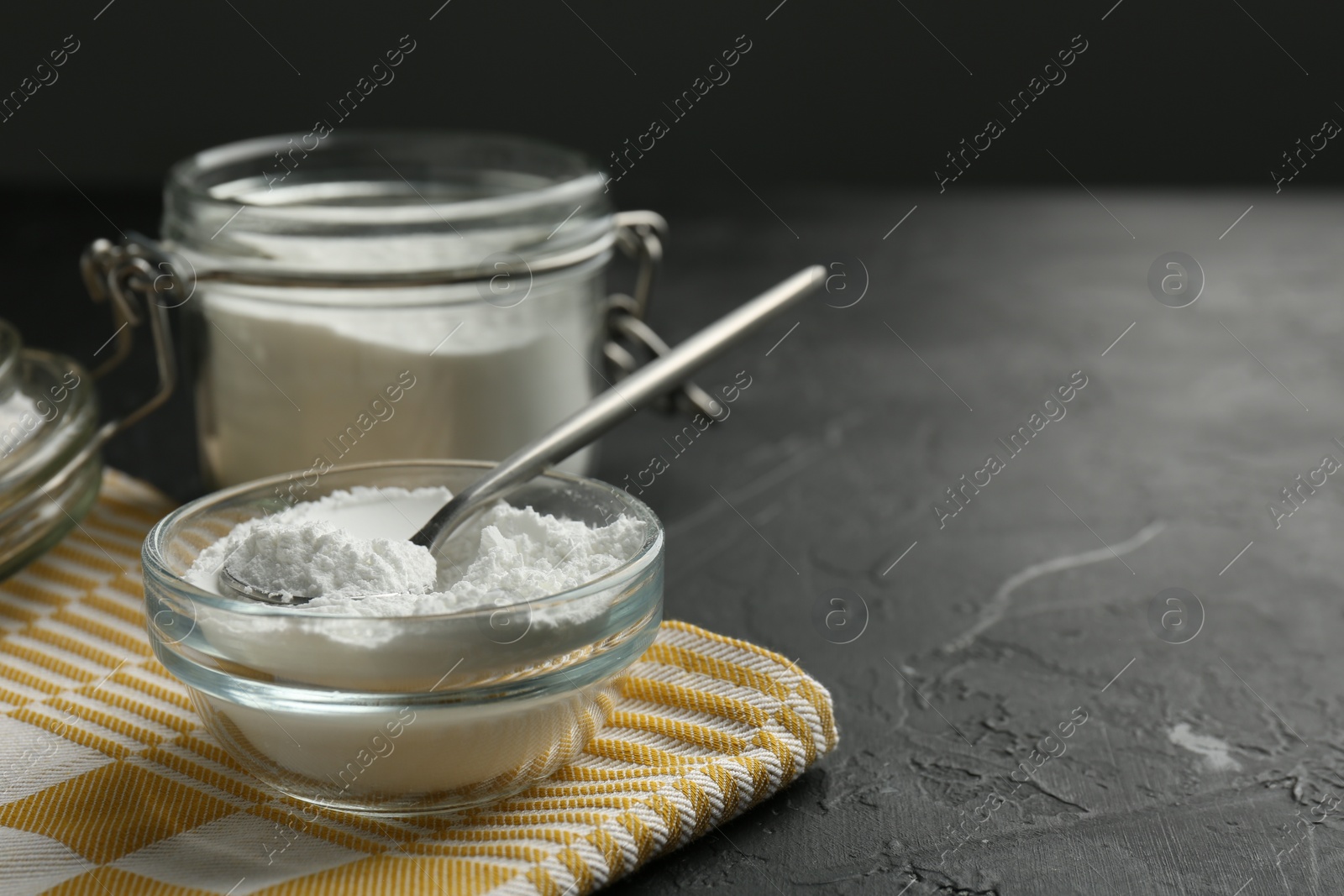 Photo of Baking powder in bowl, jar and spoon on black textured table, closeup. Space for text