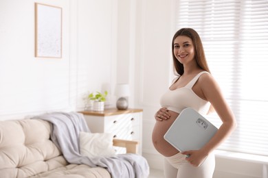 Photo of Young pregnant woman with scales at home. Space for text