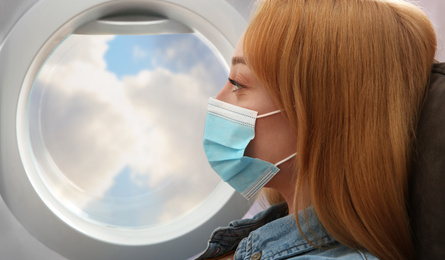 Traveling by airplane during coronavirus pandemic. Woman with face mask near porthole