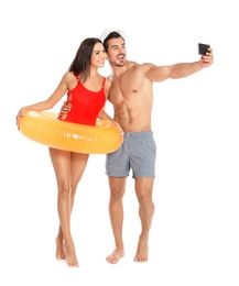 Photo of Young attractive couple in beachwear with inflatable ring taking selfie on white background