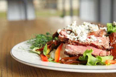 Photo of Delicious salad with roasted meat and vegetables served on wooden table indoors, closeup