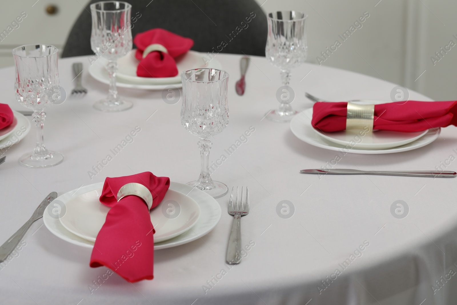 Photo of Color accent table setting. Glasses, plates, cutlery and pink napkins on table indoors