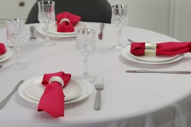 Photo of Color accent table setting. Glasses, plates, cutlery and pink napkins on table indoors