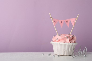 Photo of Baby shower cupcake with pink cream and Girl topper on white table against violet background, space for text