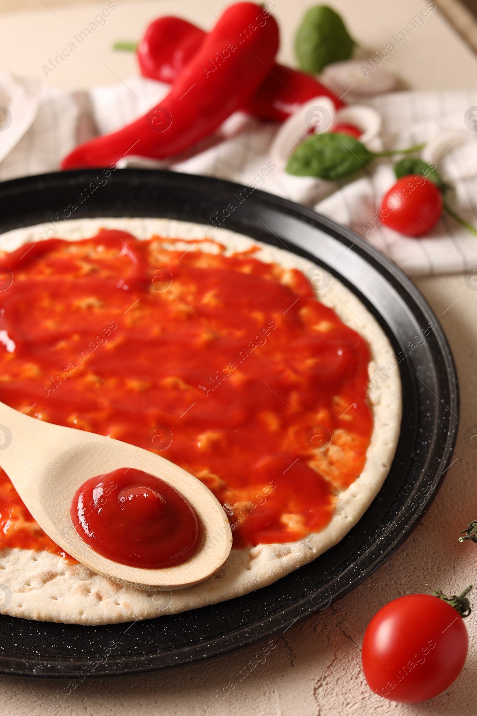 Photo of Pizza base smeared with sauce and tomatoes on light textured table, closeup