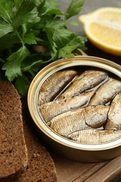 Photo of Tin can with tasty sprats served on wooden board, closeup