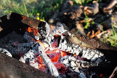 Photo of Metal brazier with burning wood outdoors, closeup