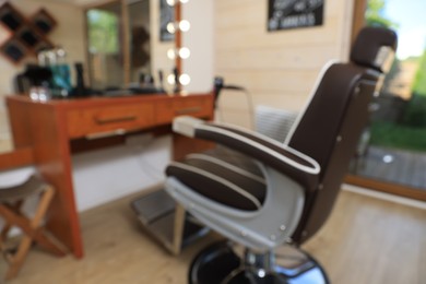 Photo of Blurred view of stylish hairdresser's workplace with professional armchair in barbershop