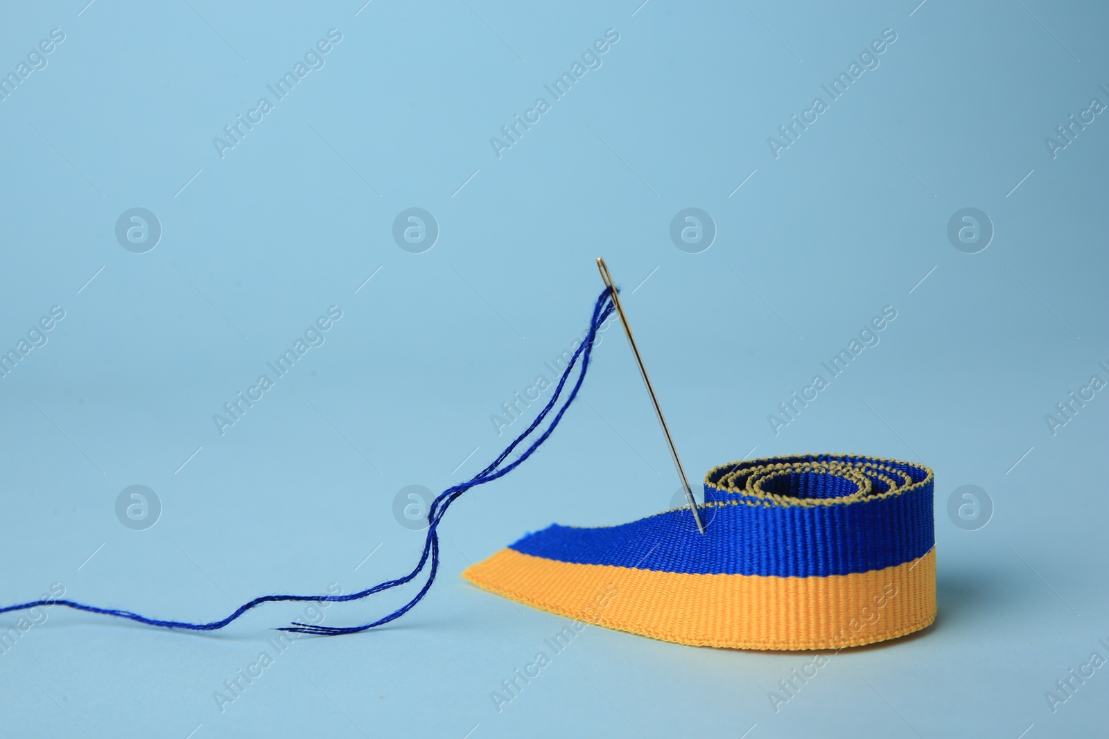 Photo of Sewing needle with thread and color ribbon on light blue background