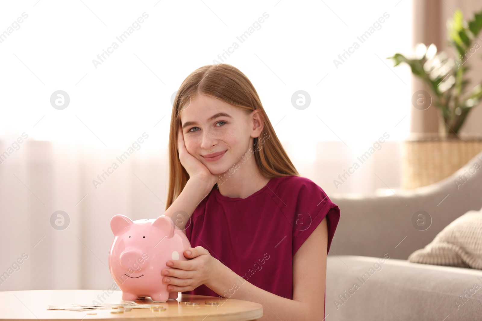 Photo of Teen girl with piggy bank and money at home