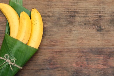 Photo of Delicious ripe bananas wrapped in fresh leaf on wooden table, top view. Space for text