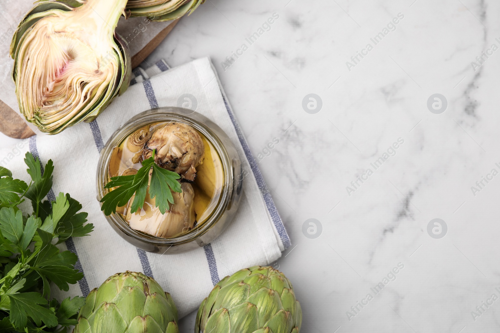 Photo of Jar of delicious pickled artichokes in olive oil and fresh vegetables on white marble table, flat lay. Space for text