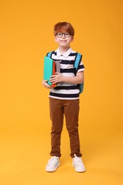 Photo of Smiling schoolboy with backpack and books on orange background