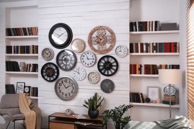 Photo of Stylish room interior with rocking chair, beautiful houseplants and collection of different clocks on white wall