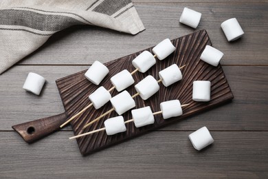 Sticks with marshmallows on wooden table, flat lay