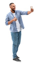 Smiling young man taking selfie with smartphone and showing thumbs up on white background