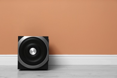Photo of Modern powerful subwoofer on floor near orange wall, space for text. Audio speaker system