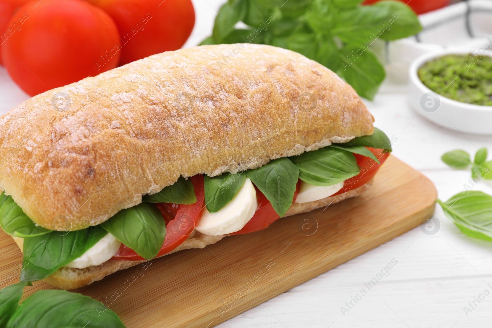 Photo of Delicious Caprese sandwich with mozzarella, tomatoes and basil on white wooden table, closeup