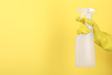 Woman holding plastic spray bottle on yellow background, closeup. Space for text