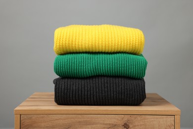 Stack of knitted sweaters on wooden table against grey background