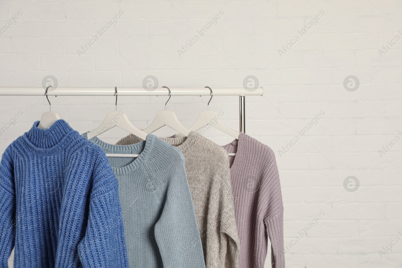 Photo of Collection of warm sweaters hanging on rack against white brick wall. Space for text