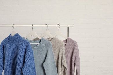 Photo of Collection of warm sweaters hanging on rack against white brick wall. Space for text