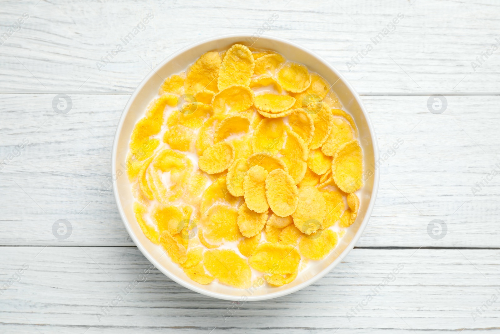 Photo of Tasty corn flakes with milk on white wooden table, top view