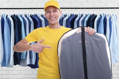 Happy courier pointing at garment cover with clothes in dry-cleaning