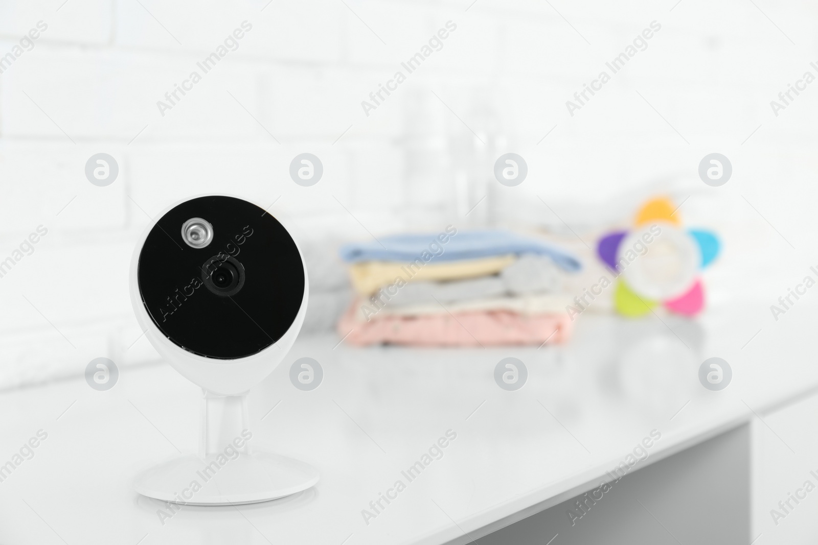 Photo of Baby camera on table near white brick wall, space for text. Video nanny