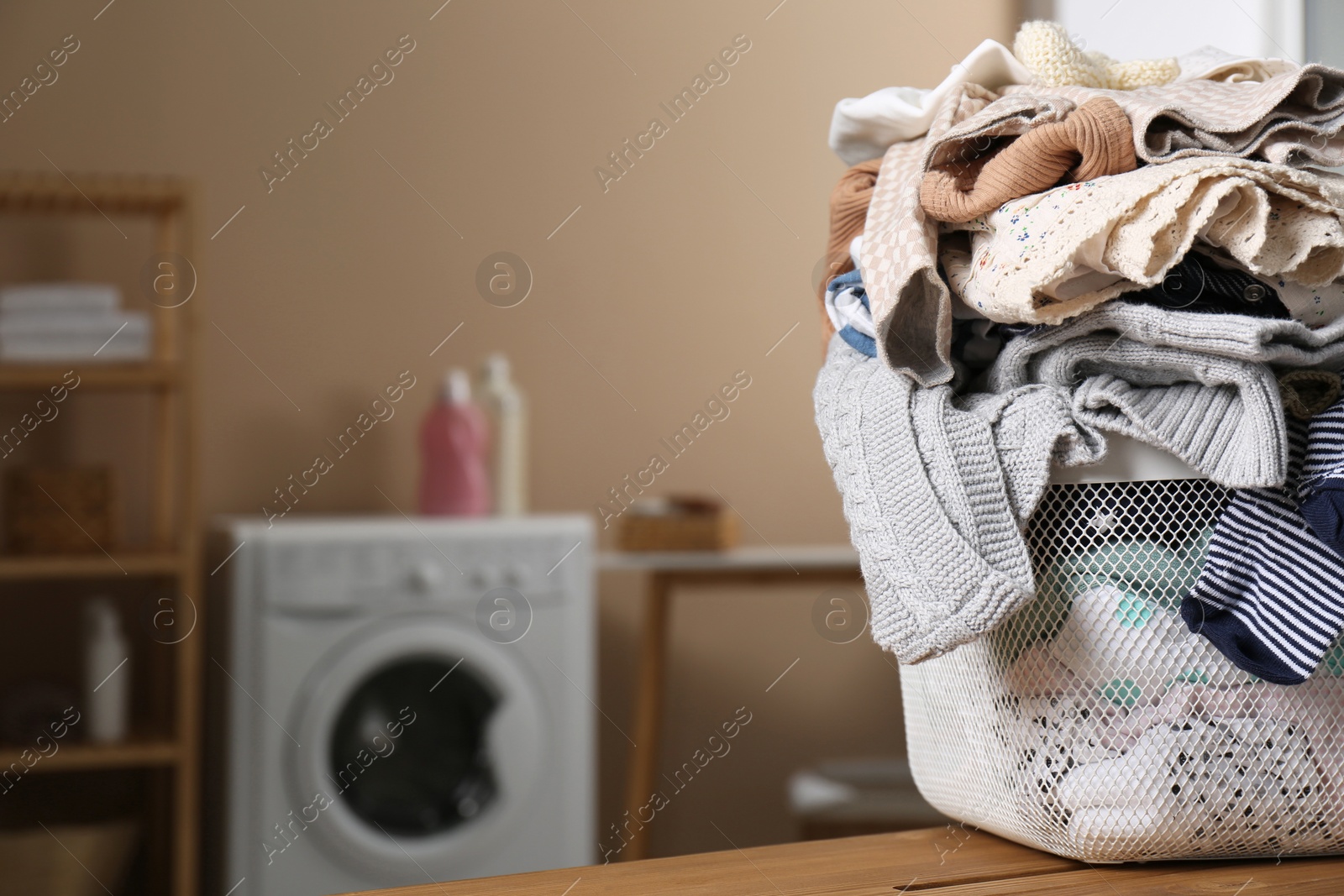 Photo of Laundry basket with baby clothes on wooden table in bathroom, space for text