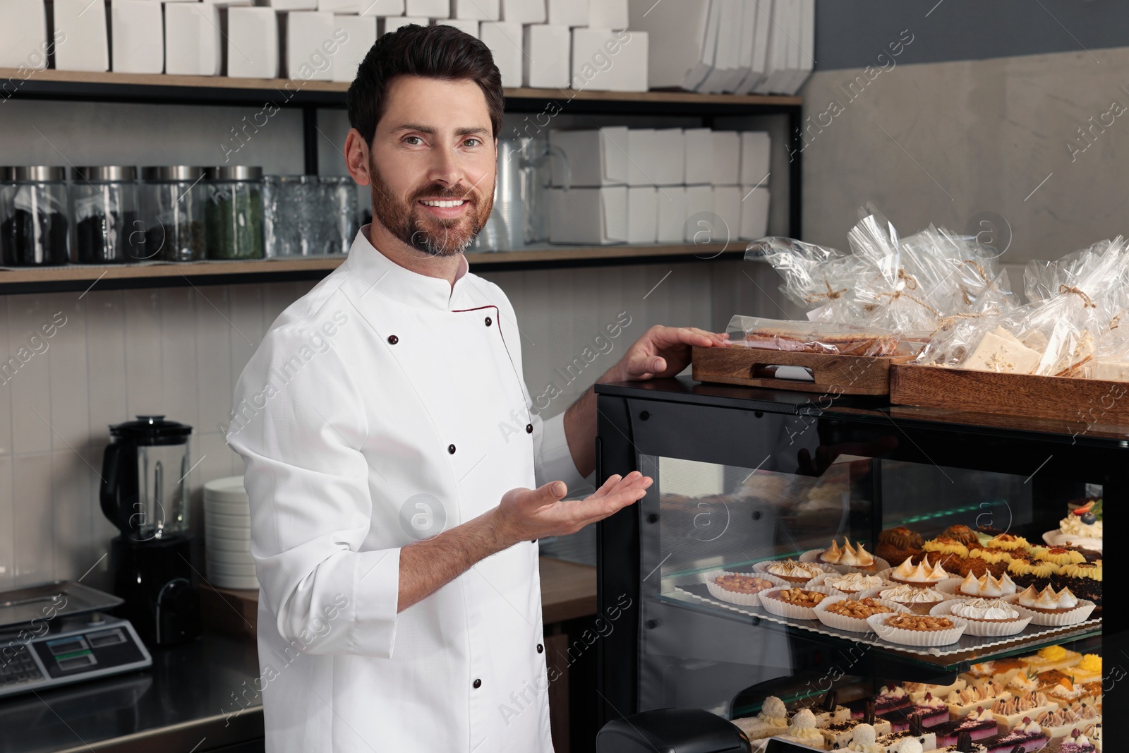 Photo of Professional baker near showcase with pastries in store