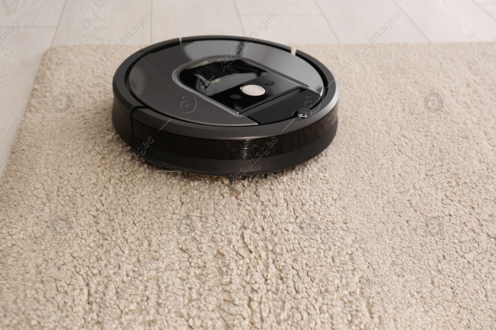 Photo of Modern robotic vacuum cleaner on beige carpet. Space for text