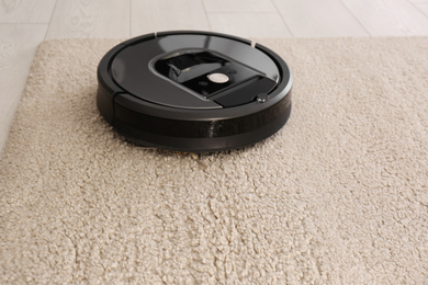 Modern robotic vacuum cleaner on beige carpet. Space for text