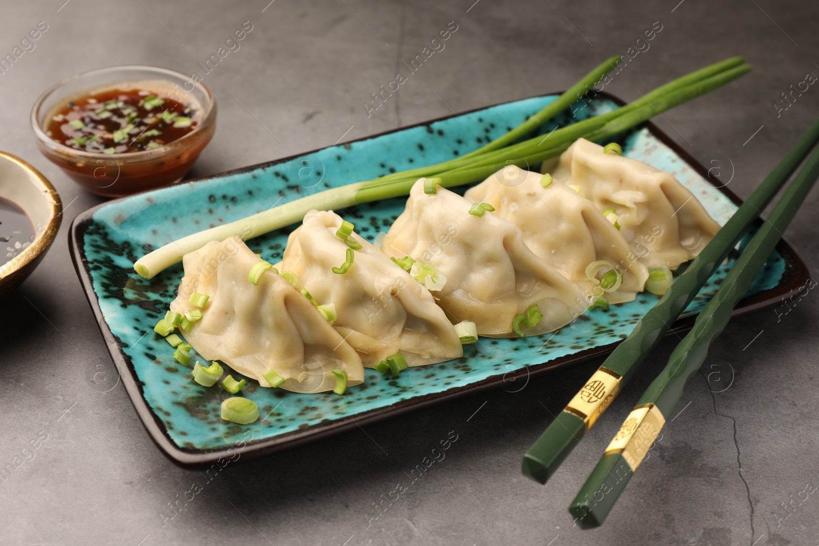 Photo of Delicious gyoza (asian dumplings) with onion and chopsticks on gray table