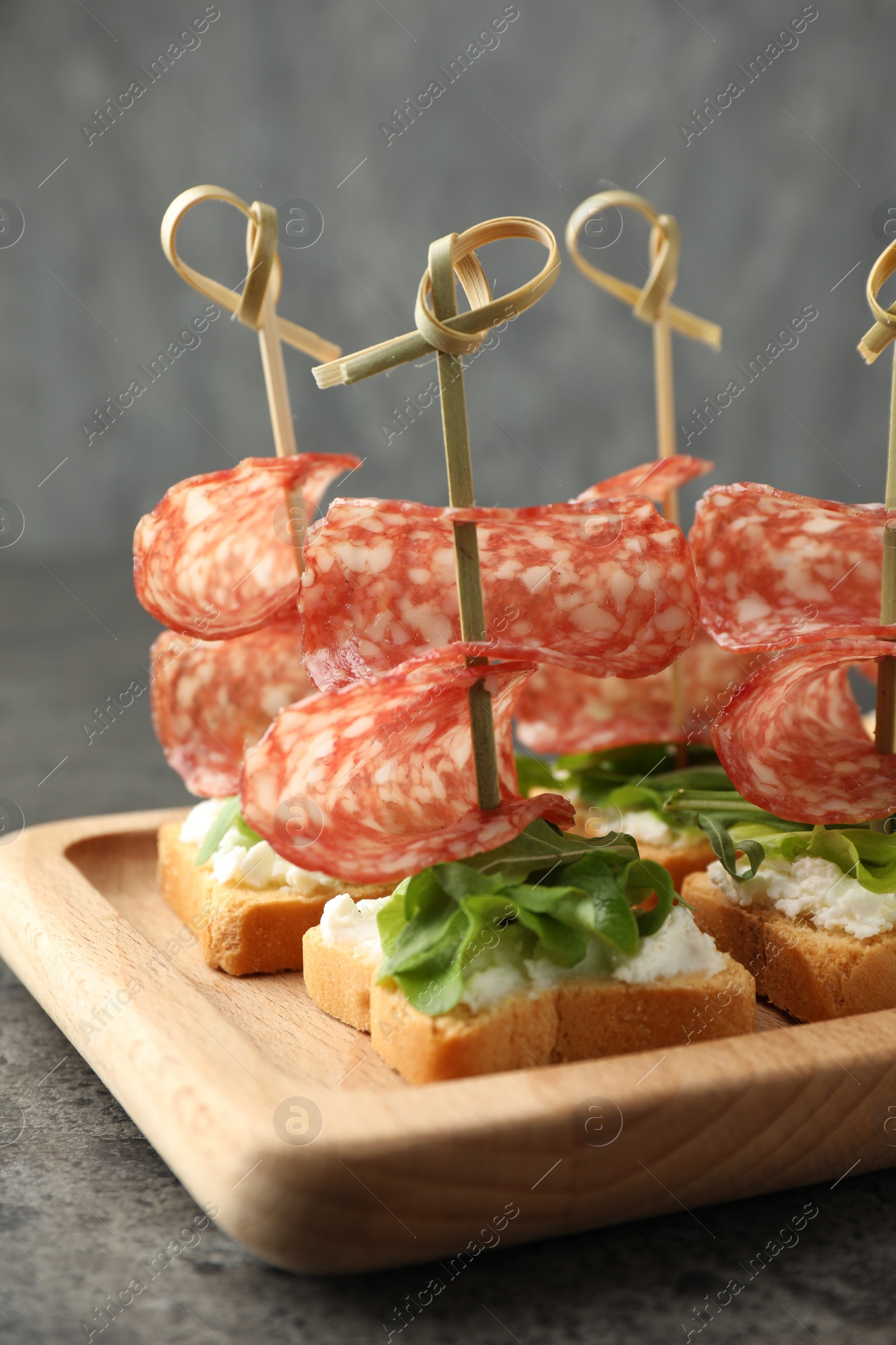 Photo of Tasty canapes with salami, greens and cream cheese on grey table, closeup