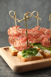 Photo of Tasty canapes with salami, greens and cream cheese on grey table, closeup