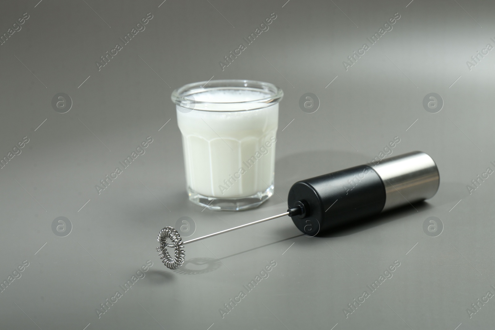 Photo of Mini mixer (milk frother) and whipped milk in glass on grey background. Space for text