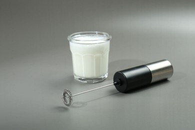 Mini mixer (milk frother) and whipped milk in glass on grey background. Space for text