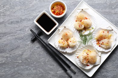 Photo of Raw scallops with spices, dill, lemon zest, shells and soy sauce on grey marble table, flat lay