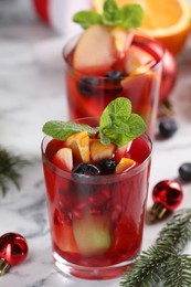 Photo of Aromatic Sangria drink in glasses, ingredients and Christmas decor on white marble table