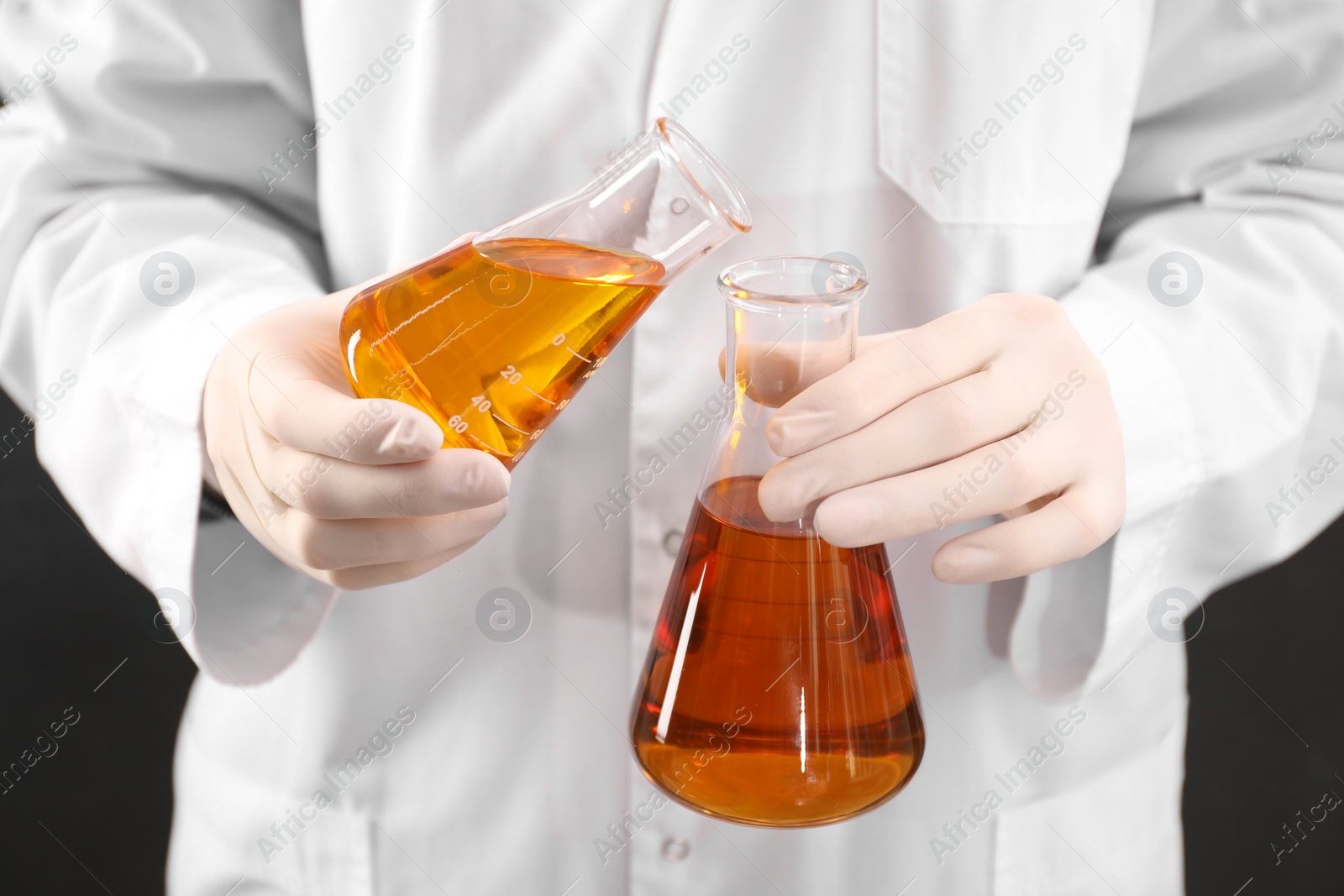 Photo of Woman pouring yellow crude oil into flask on dark background, closeup