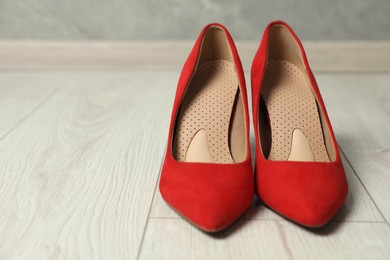 Photo of Orthopedic insoles in high heel shoes on floor, closeup. Space for text