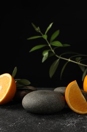Photo of Tasty fresh oranges, stones and leaves on black table, closeup